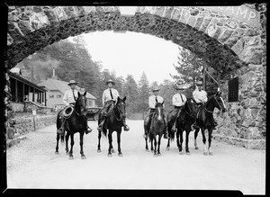 Five men on horses standing under the entrance to Big Pines Camp in winter, 1928