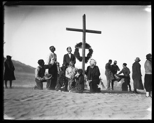 Group of people congregating around a cross at a funeral in the desert