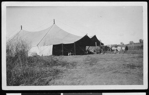 Two men standing near a large tent, ca.1910