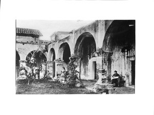 Three people on the patio and in the corridor of Mission San Juan Capistrano, ca.1895