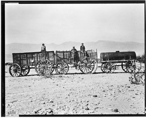 Three men standing on two wagons near a tank of water in Death Valley, ca.1900