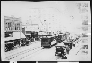 Line of trolley cars moving through a busy city, Long Beach, 1914