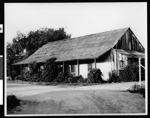 Exterior view of the Burruel adobe, its porch overgrown by bushes, San Juan Capistrano, ca.1930