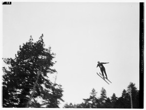 Man in skis wearing the number 82 on his sweater, soaring over the tops of trees with his arms spread,Big Pines