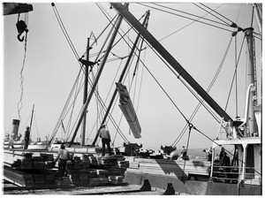 Crane loading lumber from the dock to a nearby ship at the Los Angeles Harbor