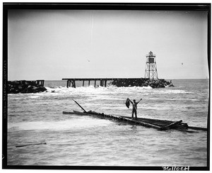 Weather beaten Long Beach breakwater partially damaged with man standing on a large peice from it which is floating in the water at right