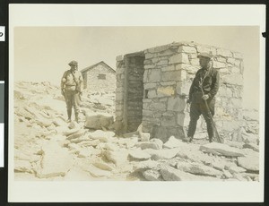 Two men amidst stone buildings on the top of Mount Whitney