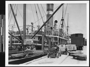 Orange crates being loaded onto a ship, showing a man driving a tractor, ca.1930