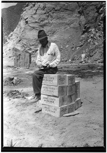 Man sitting on a crate of explosives at the construction of the San Gabriel dam, 1936