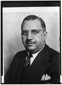 Portrait of a man with a moustache and glasses in a dark suit