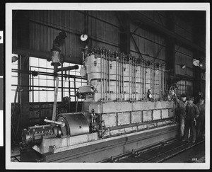 Interior view of an unidentified factory, showing three men at a large engine, ca.1940