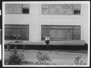 Exterior of the Robert Morton factory, showing a girl sitting on a long "bombarde pipe", ca.1925