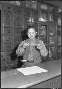 Portrait of Edward Wong using a scale in a drugstore in Los Angeles's Chinatown, November 1, 1933
