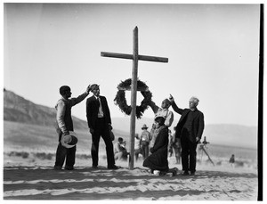 People pointing up at a cross at a funeral in the desert