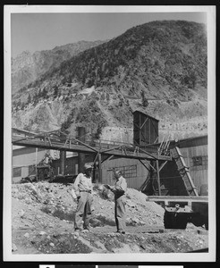 Two workers standing outside a mining facility, ca.1900