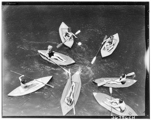 Seven women in one-person boats playing a game with a ball