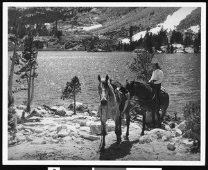 A woman on a horseback in front of a mountain lake, ca.1940