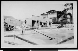 Worker floating street concrete surface with a long handled float until its initial set