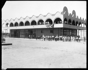 Exterior view of the Alamo Hotel in Holtville, showing a band among a larger group of people congregated in the front, 1910