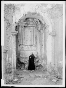 Father Superior O'Keefe standing at the old altar in the mortuary chapel at Mission San Luis Rey de Francia, August 2, 1900