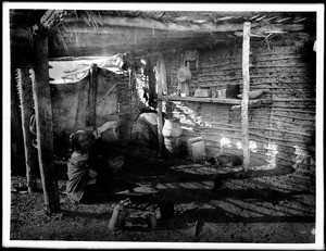 Yuma Indian woman sitting in shadow by her cooking fire in the ramada of her native dwelling, ca.1900