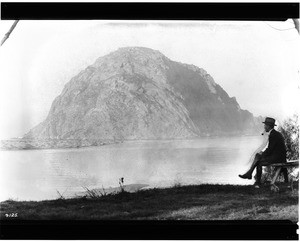 View of Morro Rock twelve miles west of San Luis Obispo, showing a man on a bench, ca.1900