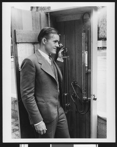 Close-up view of man adjusting plumbing in a small wooden closet, ca.1925