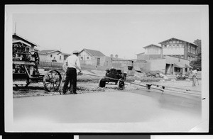 Worker applying bituminous seal coat to concrete paving (part of the Hunt curing process)