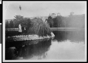 View of an Echo Park lake with two people standing on the shore, ca.1900