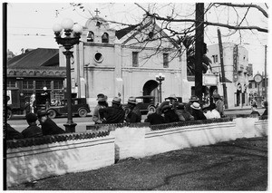 People sitting along a street across from the Plaza Church in Los Angeles