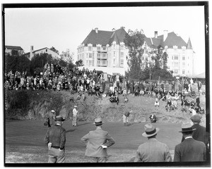 Man making a putt during a golf tournament at the Wilshire Country Club, showing a building in the background, 1931