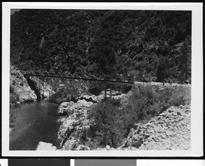 Precession of automobiles passing over a ravine bridge, ca.1930