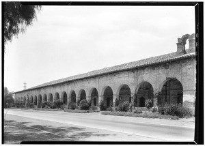 Exterior view of the San Fernando Mission, showing a street and bushes, July 29, 1927