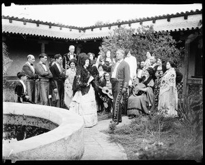 Mexican couple standing in front of a group of people, including guitar players, at a party