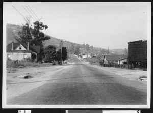 Rural town road with an oil well at distant right, ca.1930