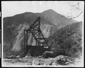 Automobile parked next to mining equipment at a mountain's edge, ca.1900