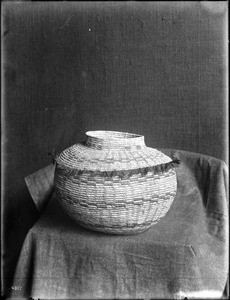 Indian basket displayed in front of a cloth backdrop, ca.1900