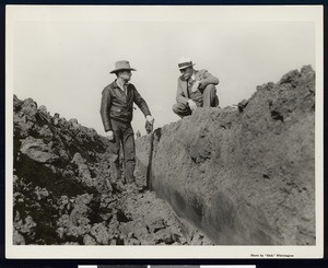 Two men examining a trough created by a "giant plow", ca.1925