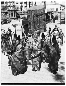 Procession of fourteen Chinese individuals in fancy dress, marching down Lotus Pool Road