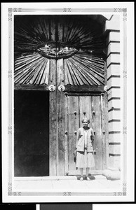 Woman outisde a large wooden doorway in Mexico, ca.1905