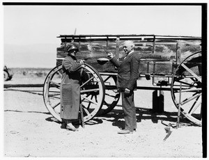 Man and woman pointing guns at each other in front of a wagon
