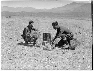 Two men bent over the grave of Tim Ryan in the desert