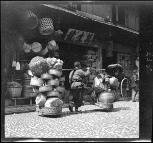 Basket vendor moving along a cobblestone street in China, ca.1900