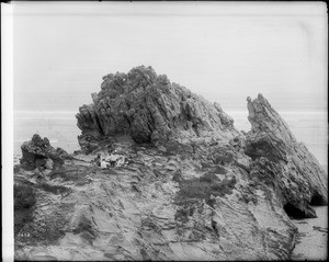 Reverend B. Fay Mills, his wife, and Dr. George Wharton James "and friends" picnicking on large rocks at Corona del Mar Beach, ca.1900