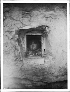 Small Hopi Indian child peering out a window, ca.1900