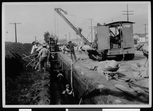 Workers constructing a storm drain along an unidentified road