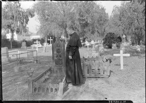 Priest or monk staring down at a grave at the San Gabriel cemetery, December 4, 1929