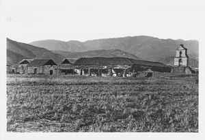 View of Mission Asistencia of San Antonio at Pala showing stubble field in front and hills behind, ca.1870-1880