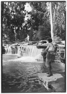 Jewell Teegardin fishing on a rock above the falls and Beatrice Williams fishing in the foreground, Rainbow Angling Club, Azusa, October 1930