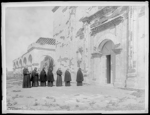 Group of monks lined up outside about to enter the church at Mission San Luis Rey de Francia, August 2, 1900